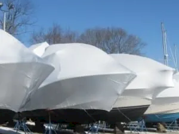 This image shows several boats covered in white shrink wrap, likely in dry storage for the winter, with a clear blue sky in the background.